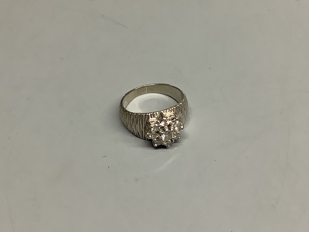 A modern textured white metal and diamond cluster set dress ring